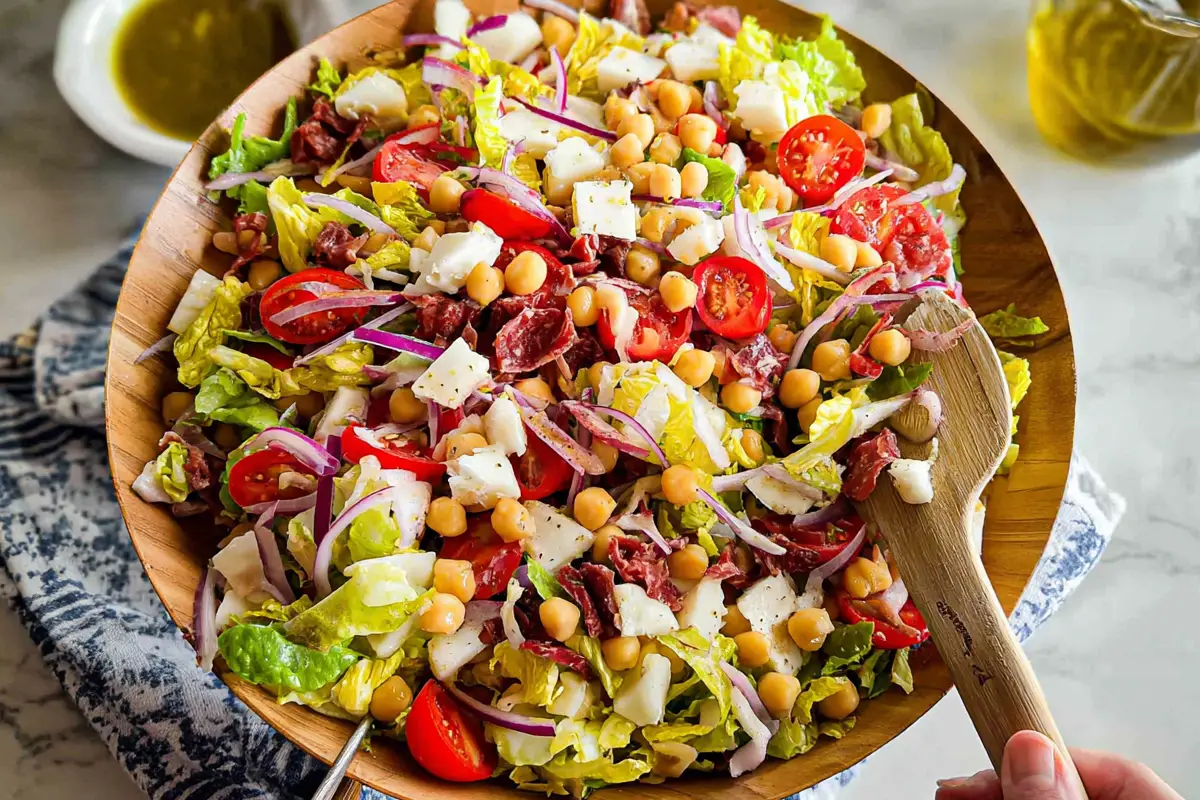 Colorful Italian Chopped Salad with cherry tomatoes, chickpeas, mozzarella, red onions, and romaine lettuce in a wooden bowl with a spoon.