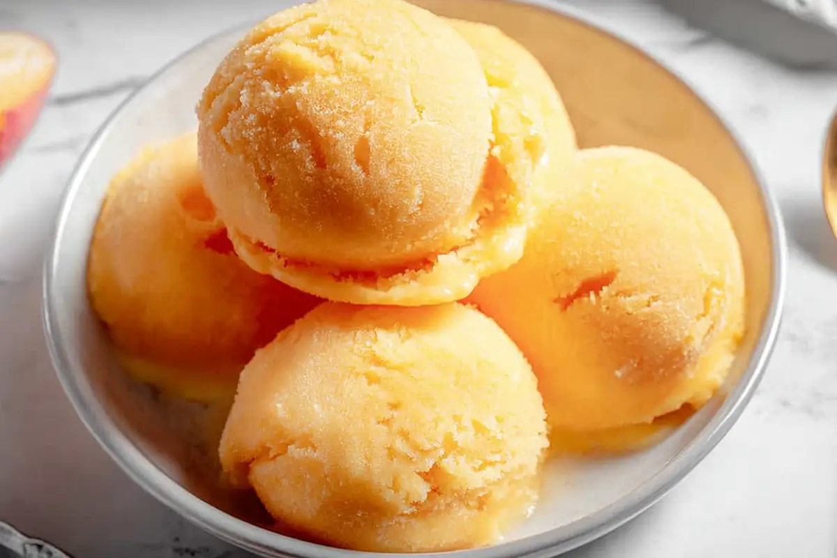 A bowl filled with five perfectly rounded scoops of peach sorbet, showcasing the creamy texture and vibrant orange hue of this refreshing peach sorbet recipe.